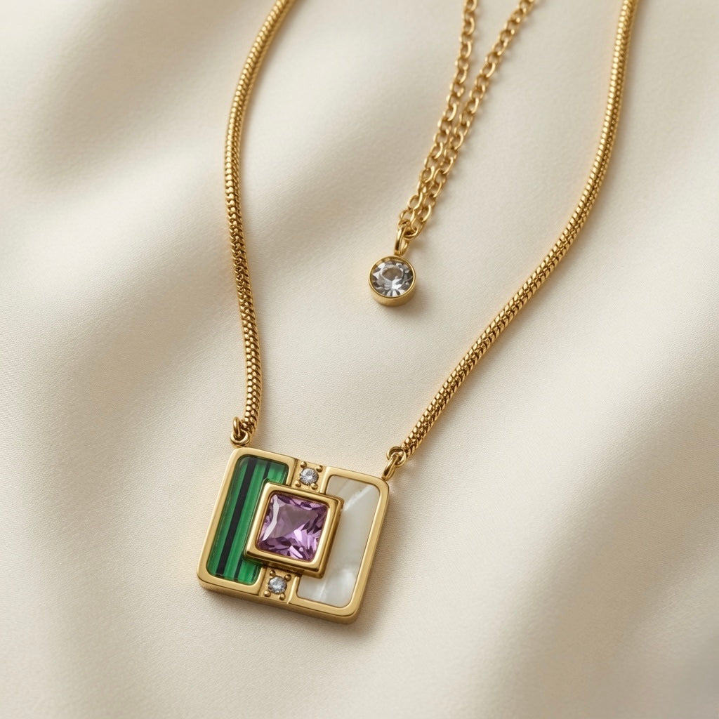 Malachite Amethyst Square Layer Necklace Set - macro close-up on ivory silk showing large square inlay pendant with deep green malachite banding upper-left quadrant, white mother-of-pearl lower-right quadrant, princess-cut lavender amethyst in raised square gold bezel at stone intersection flanked by two crystal zirconia accents, with round crystal solitaire bezel drop on cable chain above
