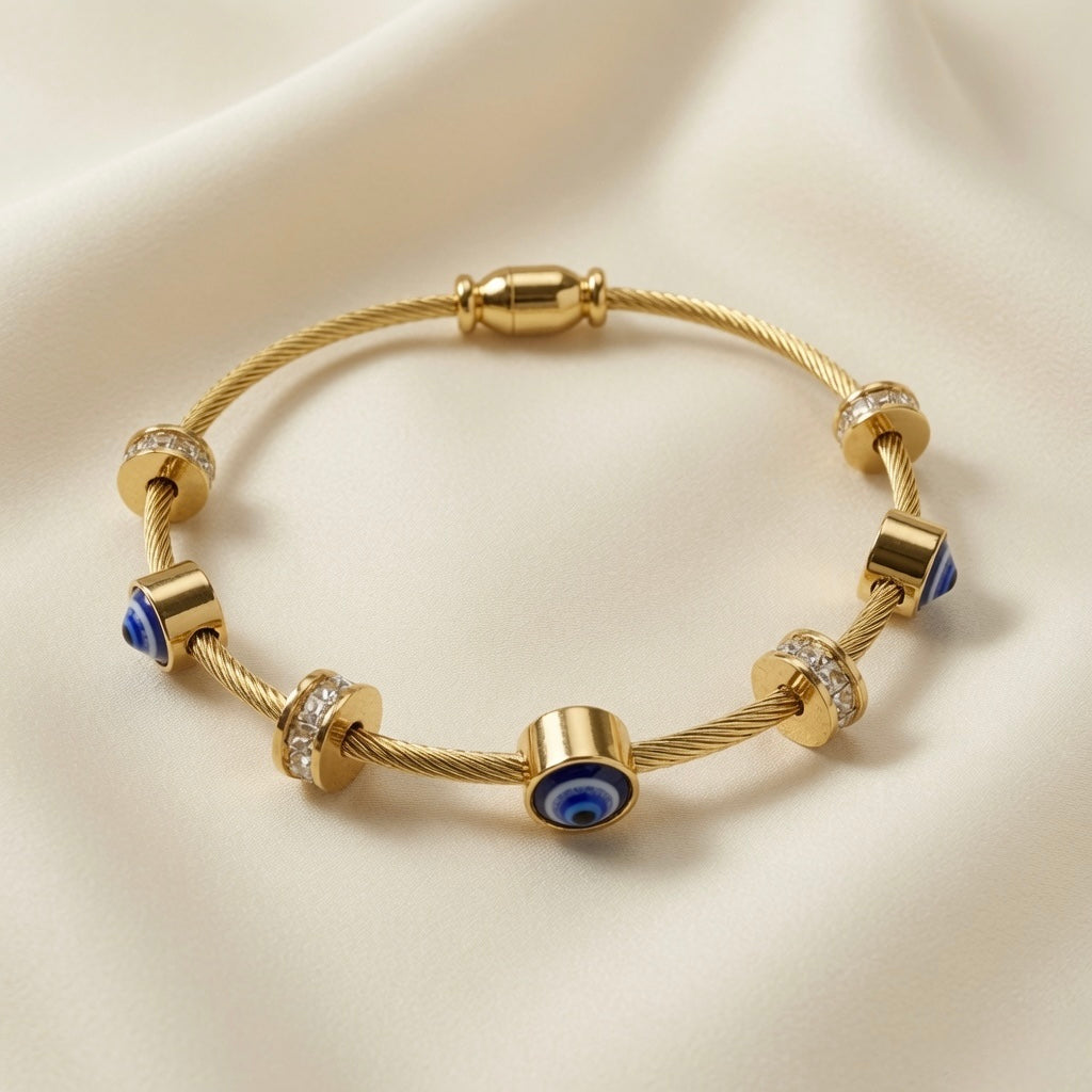 Nazar Cable Wire Evil Eye Station Bangle - close-up flat lay on ivory silk showing twisted gold cable wire bangle detail with deep blue evil eye disc stations showing navy blue iris, white ring and black pupil in gold barrel bezels, crystal pavé rondelle stations with brilliant-cut crystal zirconia and gold disc collars, gold barrel magnetic clasp
