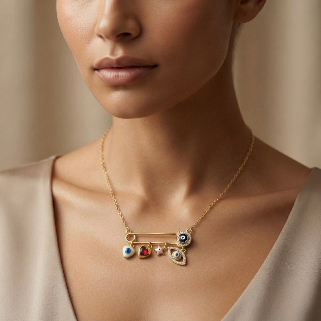 Amour Nazar Pin Charm Necklace - worn on model collarbone against nude silk dress showing gold safety pin with navy pavé evil eye at clasp, five sliding charms: white evil eye heart, ruby crystal heart, pink star and large pavé marquise evil eye hanging below pin bar on delicate gold cable chain
