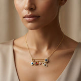 Amour Nazar Pin Charm Necklace - worn on model collarbone against nude silk dress showing gold safety pin with navy pavé evil eye at clasp, five sliding charms: white evil eye heart, ruby crystal heart, pink star and large pavé marquise evil eye hanging below pin bar on delicate gold cable chain