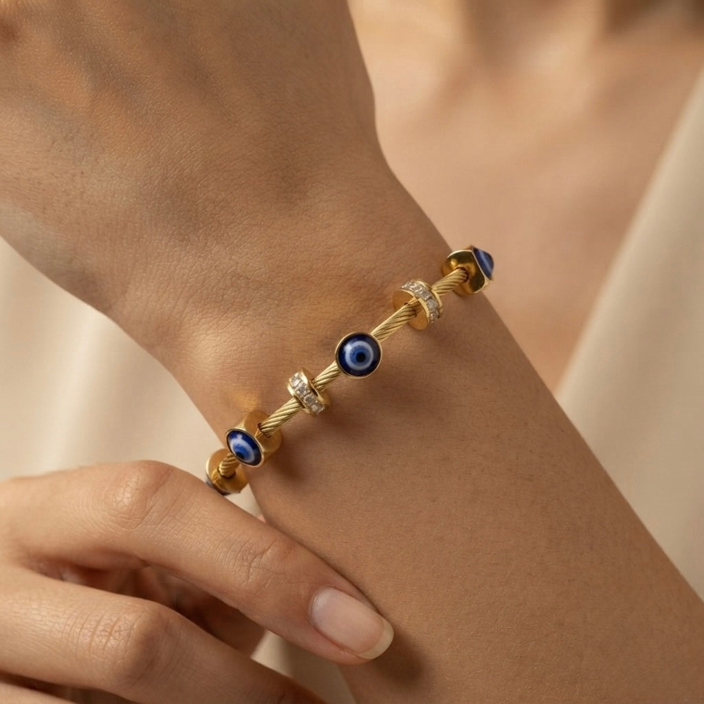 Nazar Cable Wire Evil Eye Station Bangle - worn on model wrist showing three deep blue evil eye disc stations watching outward from front, left and right of wrist simultaneously, alternating with three crystal pavé rondelle stations on twisted gold cable wire bangle against warm skin