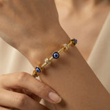 Nazar Cable Wire Evil Eye Station Bangle - worn on model wrist showing three deep blue evil eye disc stations watching outward from front, left and right of wrist simultaneously, alternating with three crystal pavé rondelle stations on twisted gold cable wire bangle against warm skin