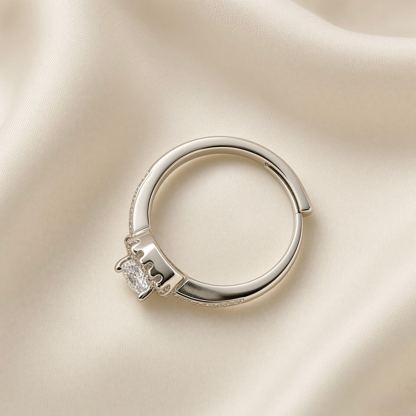 Éclat Wide Band Solitaire Adjustable Ring - three-quarter overhead view on ivory silk showing wide rhodium-plated band with open-back adjustable mechanism, micro-pavé crystal zirconia accents along both shoulders and round brilliant crystal zirconia solitaire in four-prong low-profile setting