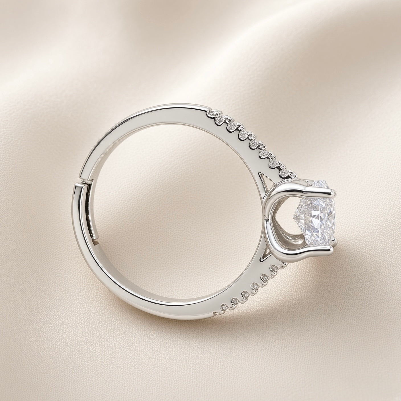 Lumière Solitaire Pavé Adjustable Ring - overhead side profile on champagne silk showing open-back adjustable band mechanism at base, pavé crystal zirconia accents along both shoulders, four-prong cathedral setting with round brilliant crystal zirconia solitaire, rhodium-plated silver-tone band