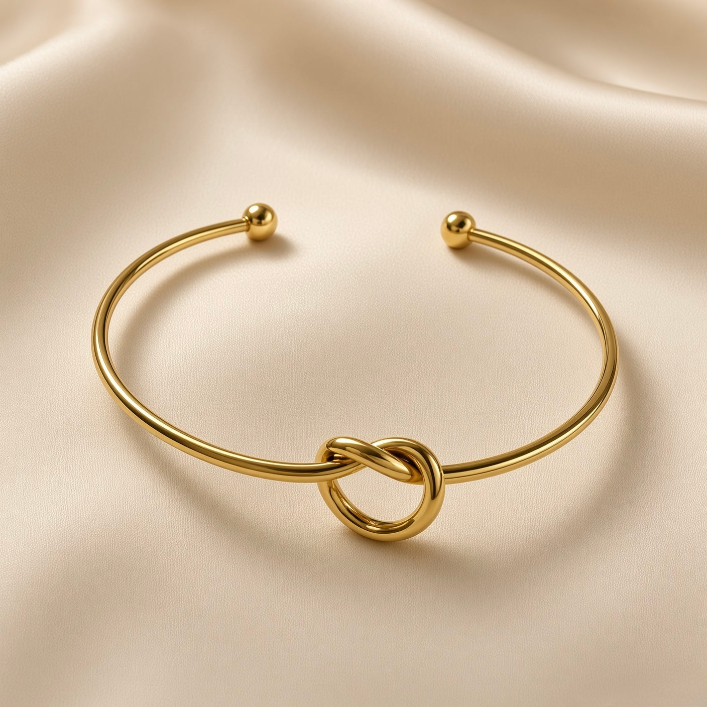 Nœud d’Amour Love Knot Ball-End Cuff Bangle - three-quarter view on ivory silk showing love knot detail at base of smooth round-wire gold open cuff bangle with two polished gold ball finials at open ends, warm 18K gold mirror-polish surface