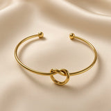 Nœud d’Amour Love Knot Ball-End Cuff Bangle - three-quarter view on ivory silk showing love knot detail at base of smooth round-wire gold open cuff bangle with two polished gold ball finials at open ends, warm 18K gold mirror-polish surface
