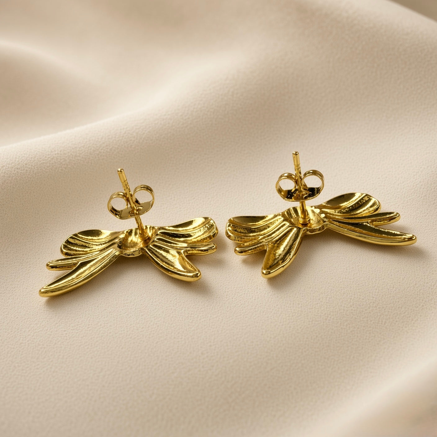 Ruban Puffy Bow Stud Earrings - pair back view on champagne silk showing reverse of both large puffy bow stud earrings: standard gold posts centred on back of bow with butterfly clutch backs, warm 18K gold mirror-polish surface on reverse of lobes and tail strands