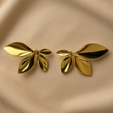 Feuilles d’Or Multi-Leaf Cluster Stud Earrings - pair front flat lay on champagne silk showing both five-leaf cluster stud earrings in warm 18K gold: one large dominant leaf extending horizontally outer, one medium leaf upward outer, one small pointed leaf top centre, two narrow leaves fanning downward, all radiating from single central point with deep shadow recesses between leaves