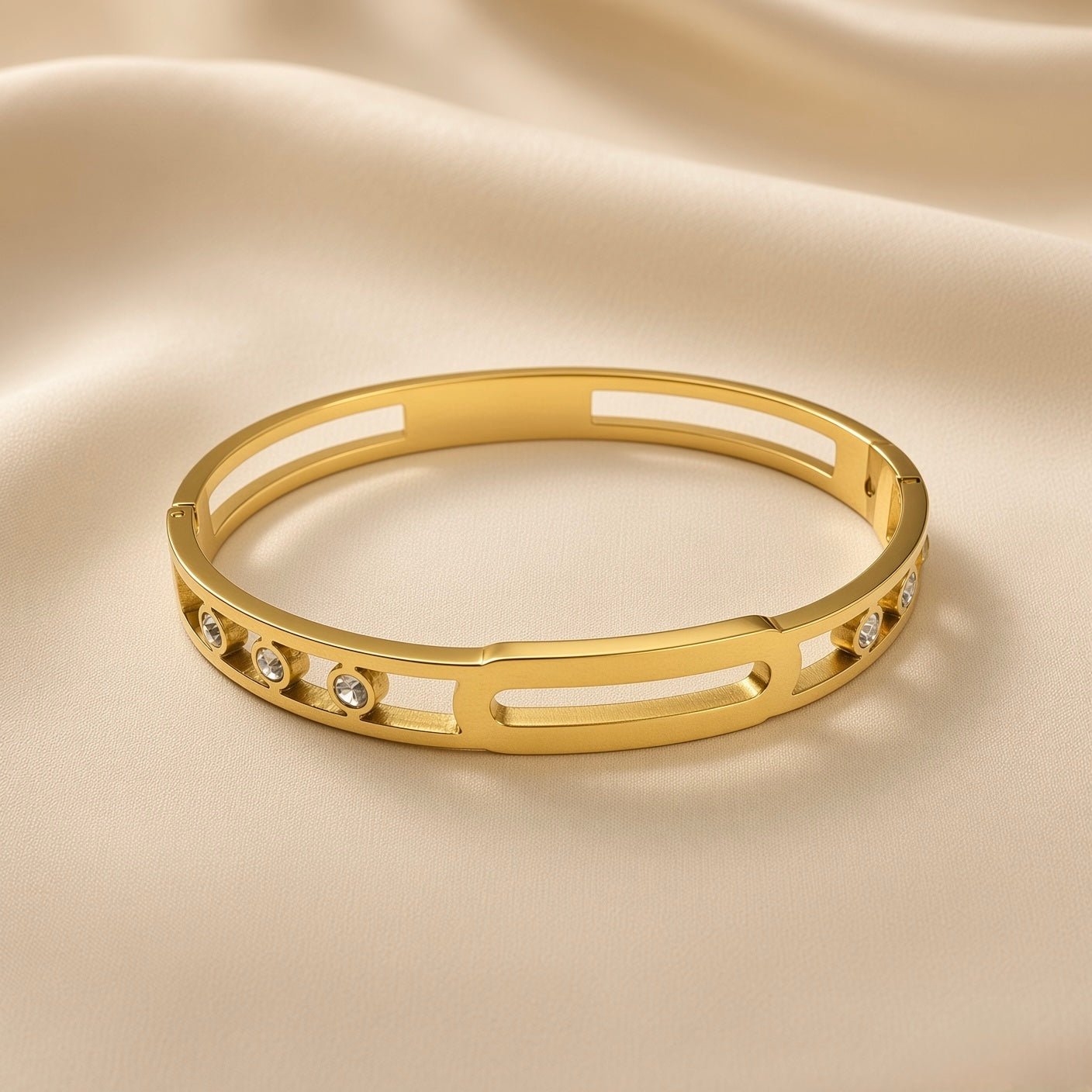 Arcade Crystal Lattice Hinged Bangle Set - crystal bangle three-quarter overhead view on champagne silk showing wide flat-band hinged bangle in warm 18K gold with open-work geometric lattice of alternating rectangular and oval cut-outs, five bezel-set round crystal zirconia stones in smooth cylindrical gold bezels evenly distributed across front arc, hinged clasp at back
