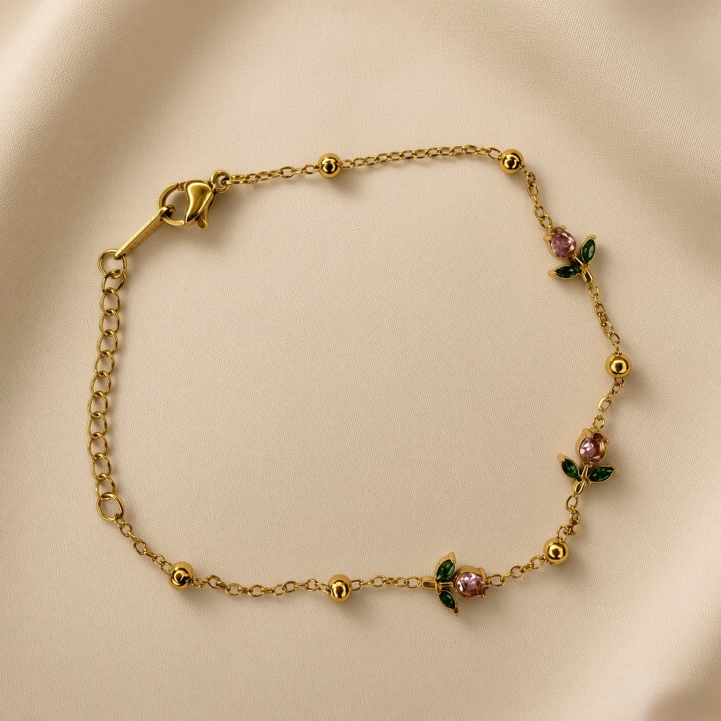 Rosette Bud Station Chain Bracelet - worn on model wrist showing bracelet in circular form: fine gold cable chain with gold ball stations and three rose bud charm stations with round rose-pink faceted crystals and dark green enamel marquise sepal elements distributed across front wrist arc, lobster clasp with extender chain visible at left
