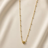 Étoile du Cœur Puffy Heart Satellite Chain Necklace - full flat lay on ivory silk showing complete necklace: fine satellite chain with smooth gold ball stations at regular intervals, three-dimensional puffy gold heart pendant with star crystal centre at bottom of chain loop