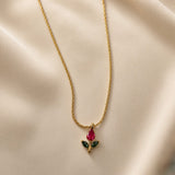 Tulipe Rouge Crystal Bud Pendant Necklace - close-up on champagne silk showing red tulip bud pendant detail: pear-cut deep ruby red crystal bud above two marquise-cut deep forest green crystal leaves on fine gold stem, fine twisted cable chain visible above smooth gold bail, deep red crystal colour and green leaf contrast clearly visible