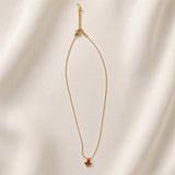Tulipe Rouge Crystal Bud Pendant Necklace - full length flat lay on ivory silk showing complete necklace laid straight: fine twisted oval-link gold cable chain with red tulip bud pendant at base showing pear-cut deep ruby red crystal bud and two marquise deep forest green crystal leaves on gold stem, lobster clasp and extender chain with small branded tag at top