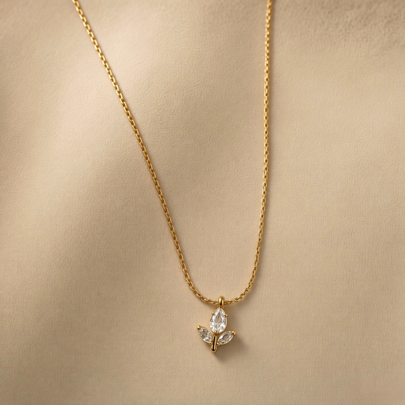 Tulipe Blanche Crystal Bud Pendant Necklace - three-quarter view on warm beige background showing complete white tulip pendant on twisted cable chain: pear-cut diamond-clear white crystal bud above two white marquise crystal leaves on fine gold stem, pure white crystal brilliance of both bud and leaves clearly visible against warm gold chain and stem