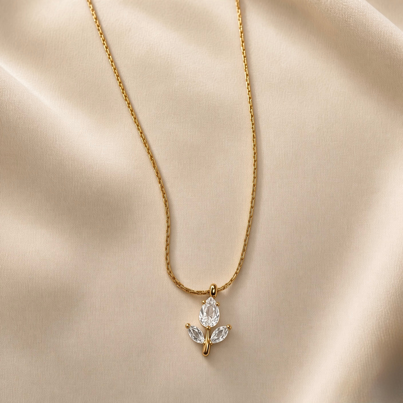 Tulipe Blanche Crystal Bud Pendant Necklace - close-up on champagne silk showing white tulip bud pendant in full detail: pear-cut diamond-clear white crystal zirconia bud in minimal gold bezel set point-downward, two marquise-cut white crystal zirconia leaves set horizontally outward from fine gold stem, smooth gold bail at top, fine twisted gold cable chain above