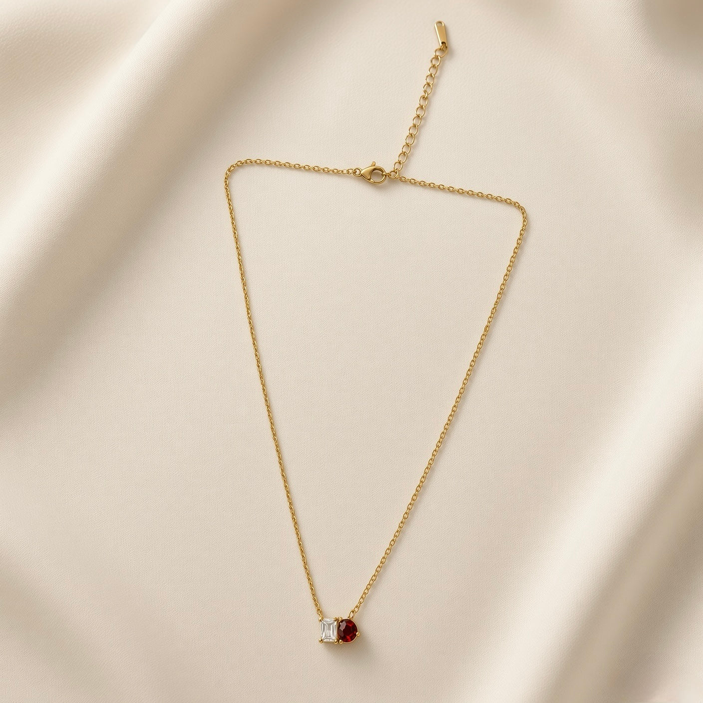 Toi et Moi Diamond Ruby Two-Stone Pendant Necklace - full length flat lay on ivory silk showing complete necklace: fine oval-link gold cable chain with toi et moi two-stone pendant at base showing princess-cut white crystal and pear-cut ruby red crystal touching at shared edge, lobster clasp and curb-link extender chain at top