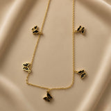 Papillon Noir Black Enamel Butterfly Charm Necklace - flat lay on champagne silk showing complete necklace in V silhouette: fine gold oval-link cable chain with five graduated black enamel butterfly charms at asymmetric intervals, two small butterflies upper sides, two medium butterflies lower sides, one large butterfly central drop pendant at bottom, deep black enamel fill with warm gold border outline on each butterfly