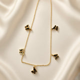 Papillon Noir Black Enamel Butterfly Charm Necklace - flat lay on ivory silk showing complete necklace in V silhouette from slightly different angle: fine gold cable chain with five black enamel butterfly charms graduated in size from small upper side butterflies to large central drop pendant, deep black enamel wings with warm gold border, lobster clasp visible at top