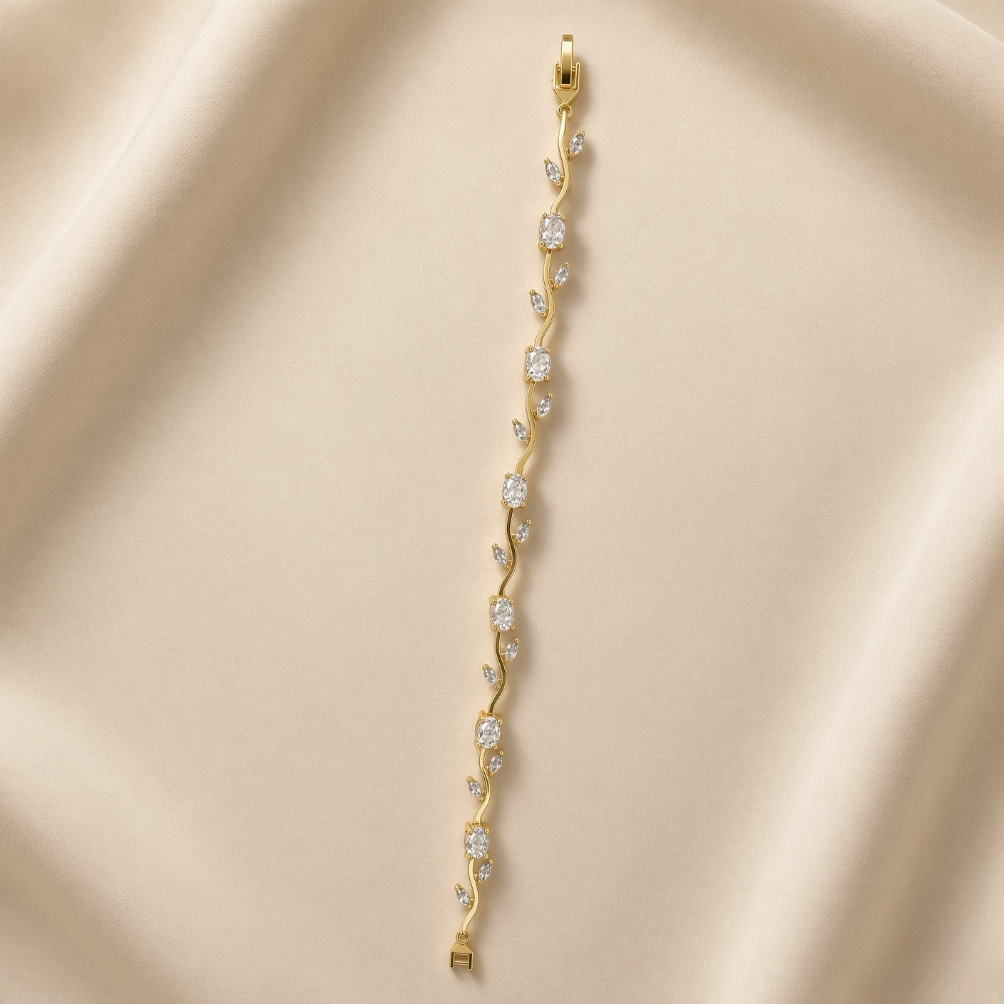 Diamant Vigne Wave Link Crystal Bracelet - full length flat lay on champagne silk showing complete bracelet laid straight: continuous sinuous S-curve gold wave links set with alternating large oval white crystal zirconia in four-prong ball-tip settings and paired marquise white crystal zirconia in two-prong settings, box clasp with safety tab at top