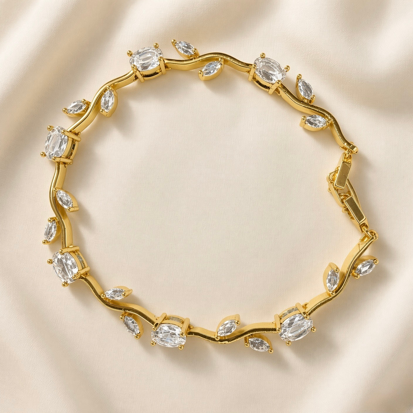 Diamant Vigne Wave Link Crystal Bracelet - circular flat lay on ivory silk showing complete bracelet in full circle: sinuous gold wave vine links with alternating large oval brilliant-cut white crystal zirconia in four-prong ball-tip settings and paired marquise white crystal zirconia in two-prong settings on wave curves, box clasp with safety tab visible at right
