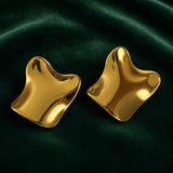 Gold Sculptural Wave Square Stud Earrings - pair elevated three-quarter view on deep forest green velvet showing both earrings from slightly above: wave-distorted square form showing full three-dimensional depth of sculptural wave, four corners curling in different directions, high mirror-polish warm gold surface reflecting deep forest green velvet background, dramatic shadow and highlight composition