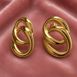 Gold Double Oval Interlocked Link Stud Earrings - pair face-on close-up on dusty pink satin showing both earrings side by side: double oval interlocked link construction in mirror-polish 18K gold, large outer oval framing smaller inner oval at centre, thick tubular walls of both ovals clearly showing three-dimensional interlock, straight post with butterfly back visible on right earring