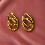 Gold Double Oval Interlocked Link Stud Earrings - pair face-on on dusty pink satin showing complete earrings from slightly wider angle: vertical oval silhouette with large outer oval and smaller inner oval interlocked, high mirror-polish warm gold surface reflecting dusty pink satin background, bold statement scale and three-dimensional chain-link construction clearly visible