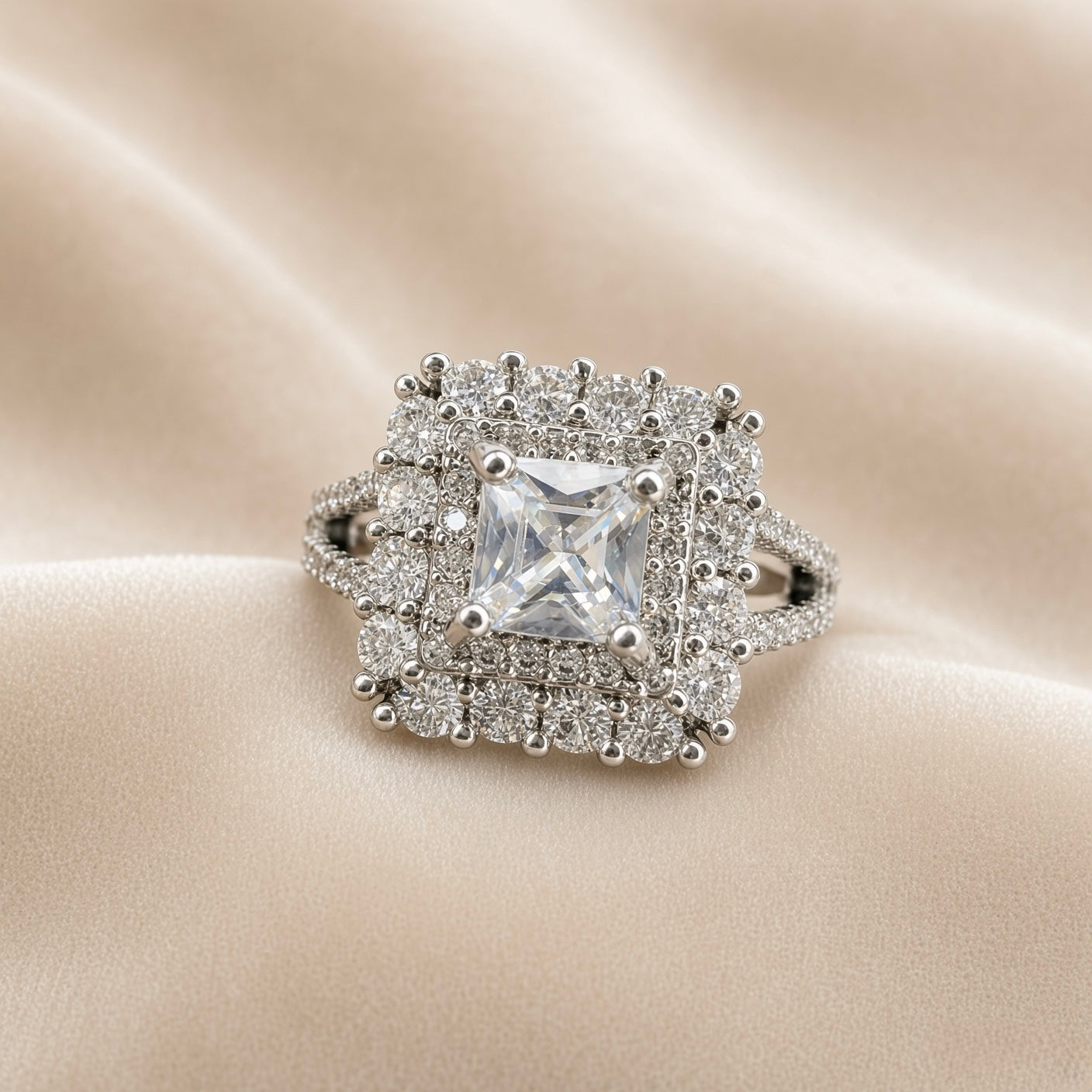 Princess Cut Double Halo Split Shank Adjustable Ring - face-on on ivory satin showing complete double halo composition: princess-cut diamond-clear white crystal zirconia centre in four-prong setting, inner halo of individually prong-set round brilliant white crystals in square arrangement, outer halo of larger round brilliant white crystals in outer square arrangement, split shank pavé band visible below