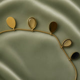 Gold Teardrop Charm Satellite Chain Anklet - macro close-up on sage green satin showing four teardrop charms in detail: solid mirror-polish warm gold flat teardrop charm (left), open gold oval bezel frame with smooth nude taupe champagne cabochon stone teardrop charm (centre left), solid mirror-polish gold teardrop charm (centre right), open gold bezel nude cabochon teardrop charm (right), fine satellite chain with gold ball stations below all charms