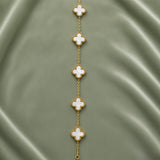 White Clover Station Bracelet Gold Milgrain - full length flat lay on sage green satin showing five clover motifs in vertical arrangement: five white mother-of-pearl four-leaf clover quatrefoil motifs with continuous milgrain gold bead borders macro detail, smooth luminous white mother-of-pearl fill and precise small gold ball milgrain border on each clover clearly visible, fine gold cable link chain connecting all five motifs