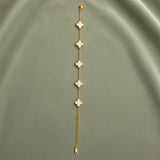 White Clover Station Bracelet Gold Milgrain - full length flat lay on sage green satin showing complete bracelet laid straight: five white mother-of-pearl four-leaf clover motifs with continuous milgrain gold bead borders evenly spaced on fine gold cable link chain, lobster clasp at top, curb-link extender chain and gold barrel tag at bottom
