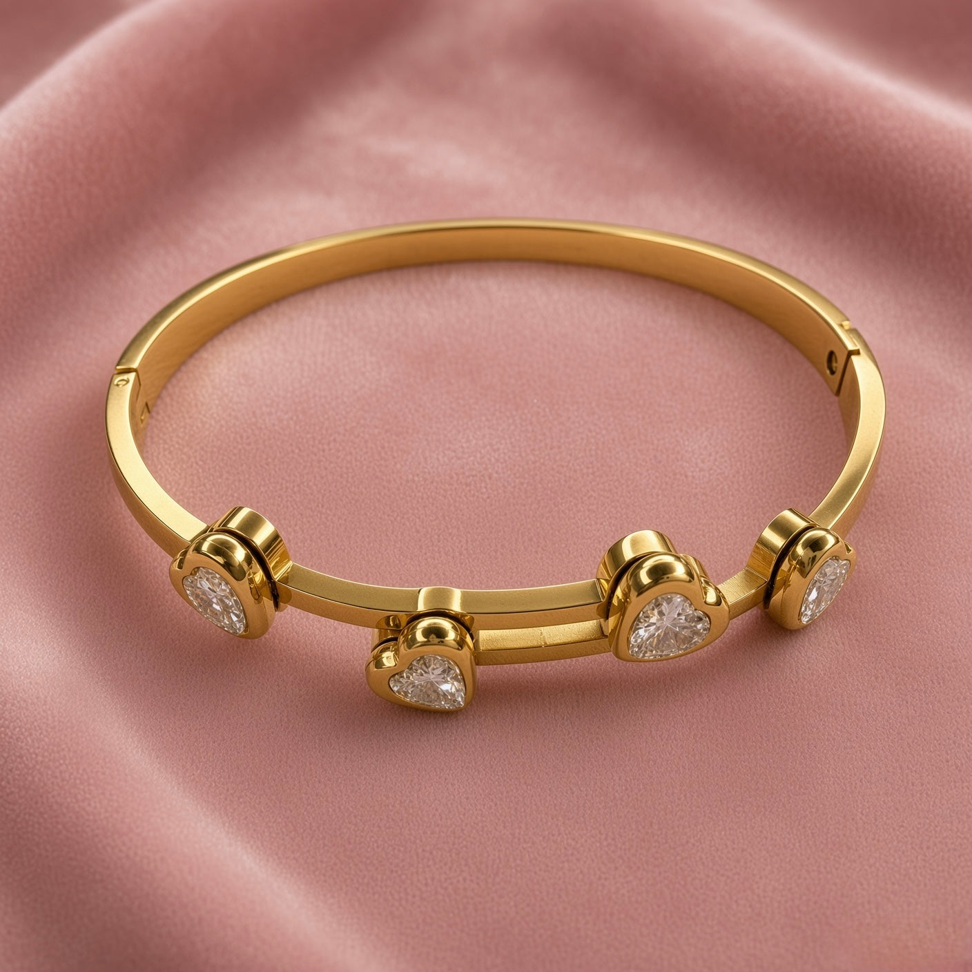 Gold-tone bracelet with four heart-shaped clear stone accents on pink fabric