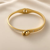 Close-up of gold-tone bangle bracelet with round clear crystal-style accents and polished band