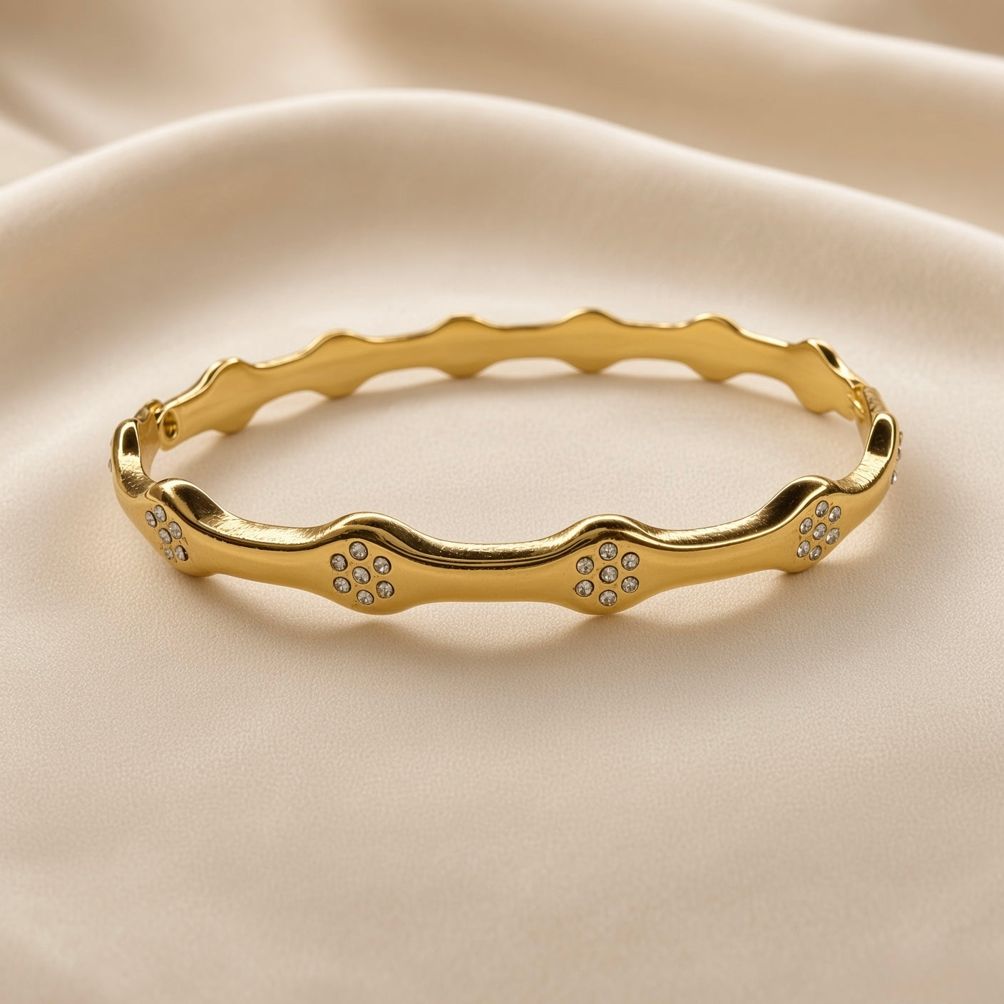 Gold-tone crystal-style wave bangle bracelet worn on a wrist