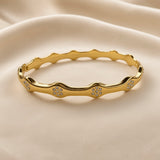 Gold-tone crystal-style wave bangle bracelet worn on a wrist