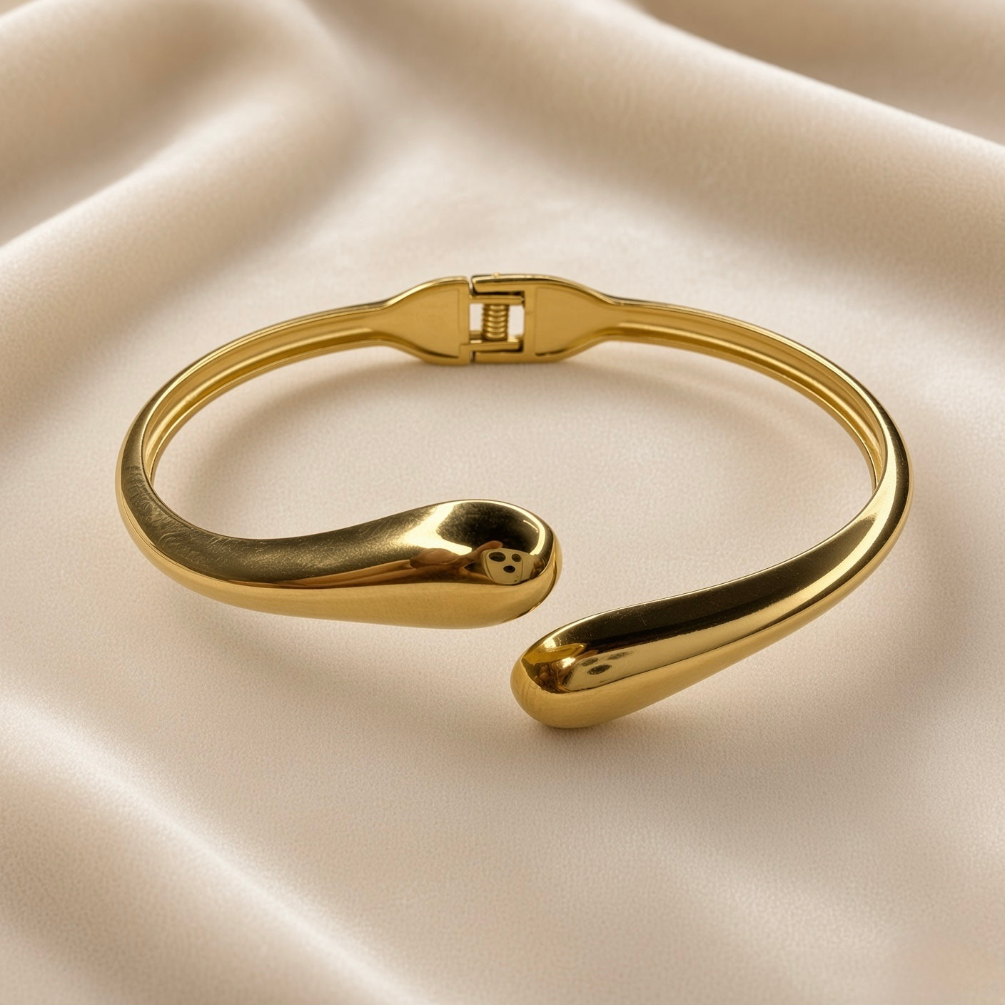 Angled view of polished gold-plated stainless steel open cuff bracelet on cream fabric