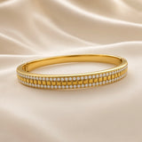 Angled view of gold-plated stainless steel clear-stone bangle bracelet on cream fabric