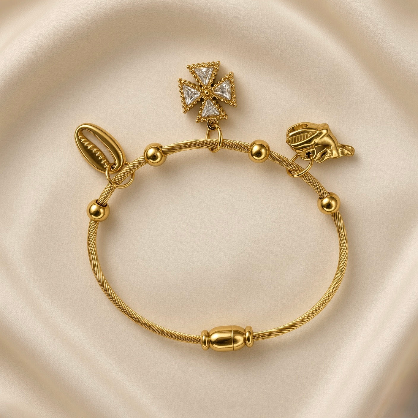 Gold-plated stainless steel charm bracelet with shell and cross pendants on cream fabric