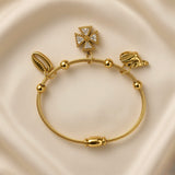 Gold-plated stainless steel charm bracelet with shell and cross pendants on cream fabric