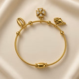 Close-up of gold-plated stainless steel charm bracelet with textured wire band and decorative charms