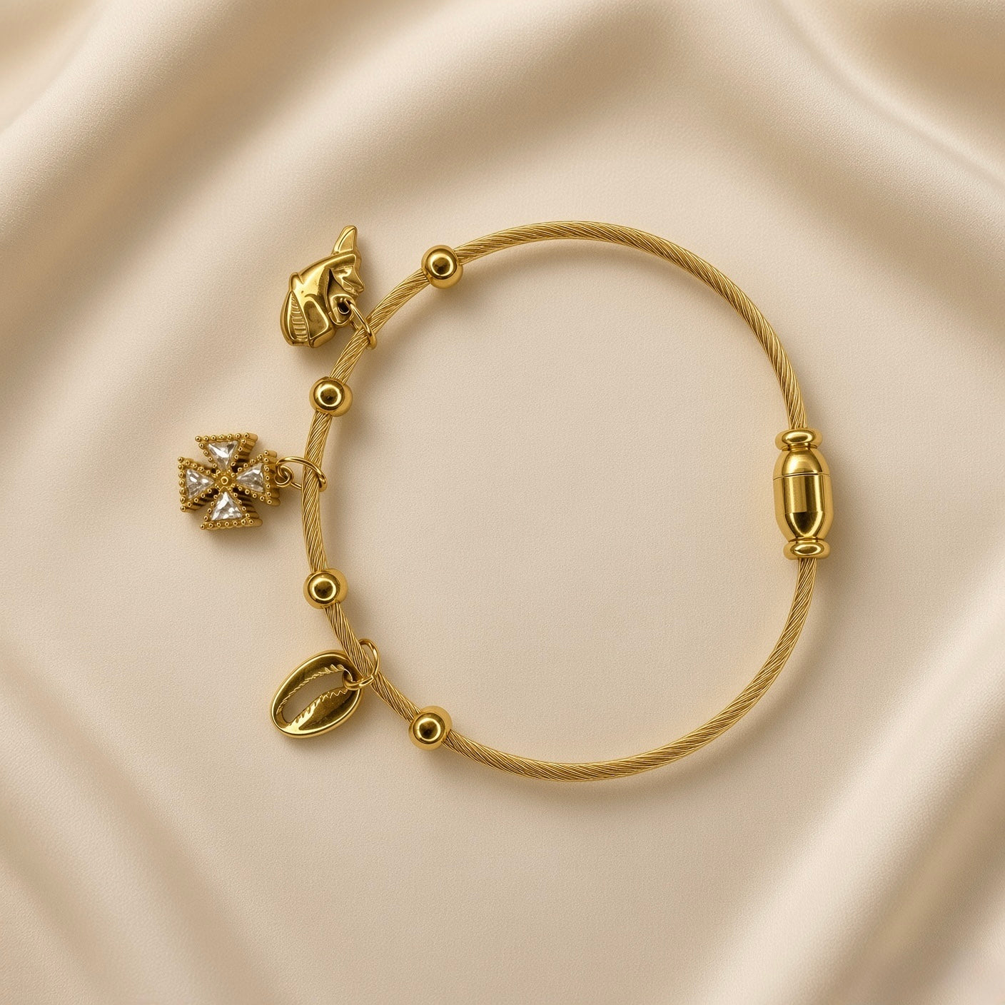 Gold-plated stainless steel charm bracelet showing shell charm, cross charm and barrel-style closure