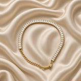 Baguette Crystal Tennis Bracelet Gold - vertical flat lay on cream satin showing full bracelet length: 30+ channel-set baguette white crystal zirconia stones edge-to-edge, gold curb extender chain at top, lobster clasp at bottom