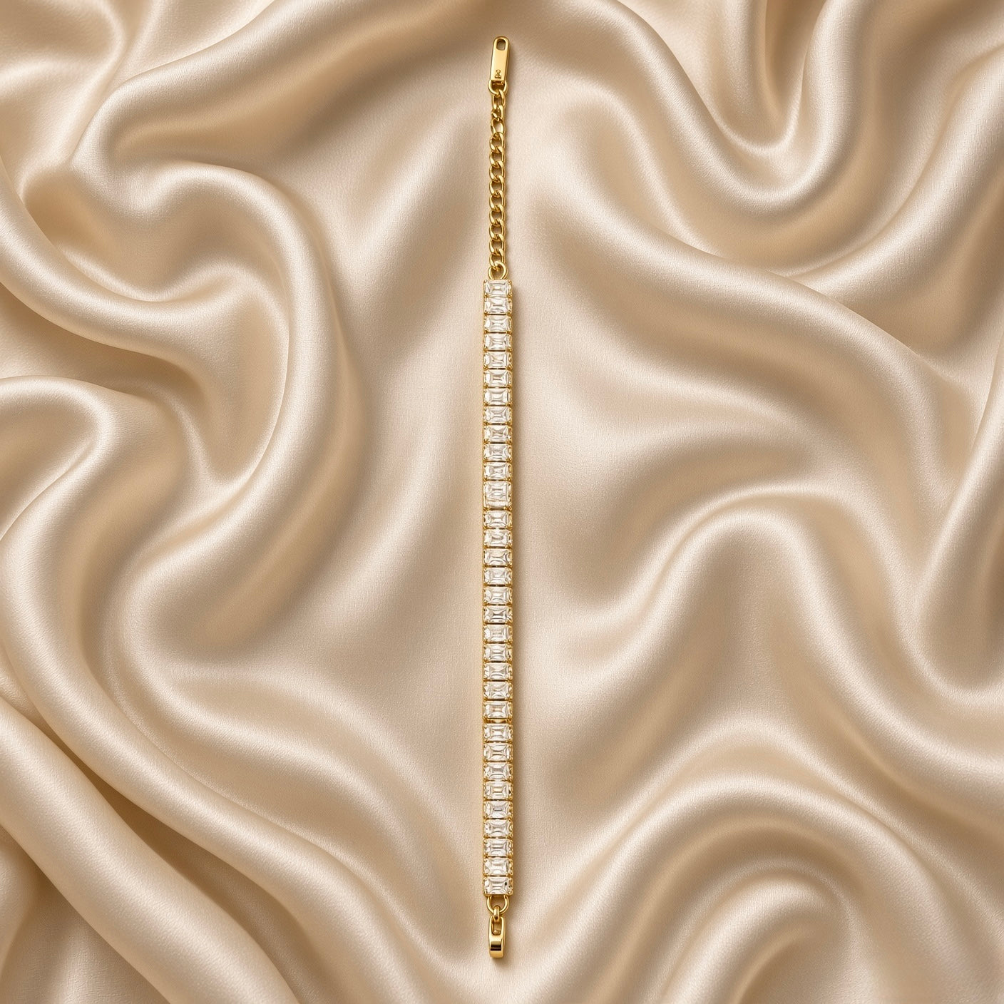 Baguette Crystal Tennis Bracelet Gold - circular flat lay on cream satin showing bracelet worn as complete wrist loop: full baguette crystal band forming continuous arc of white fire, gold curb Cuban link extender chain at bottom with lobster clasp and engraved S.steel gold rectangular tag