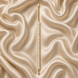 Baguette Crystal Tennis Bracelet Gold - circular flat lay on cream satin showing bracelet worn as complete wrist loop: full baguette crystal band forming continuous arc of white fire, gold curb Cuban link extender chain at bottom with lobster clasp and engraved S.steel gold rectangular tag