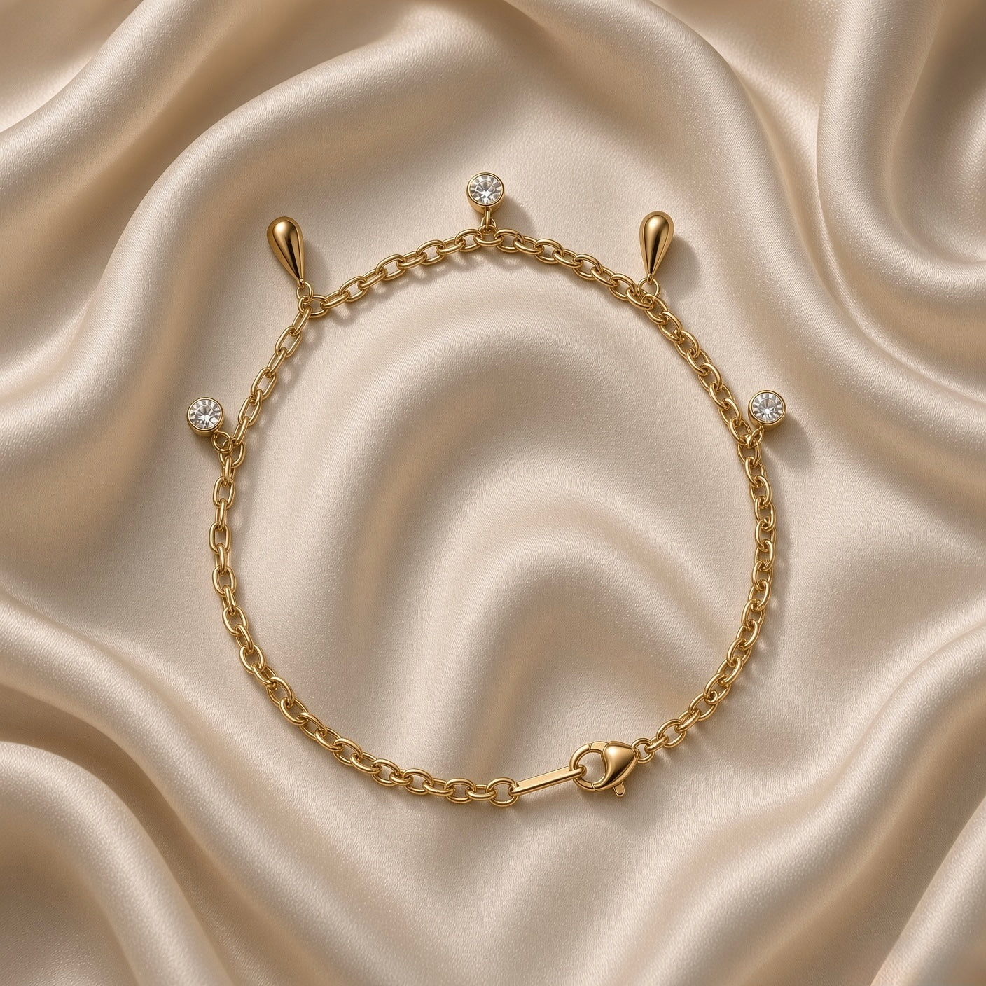 Gold Raindrop and Crystal Bezel Station Bracelet - vertical flat lay on cream satin: fine gold cable chain with five alternating dangle charms — round white crystal bezel drop at top, solid mirror-polish gold raindrop below, round white crystal bezel, solid gold raindrop, round white crystal bezel at bottom, lobster clasp at base