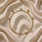 Gold Raindrop and Crystal Bezel Station Bracelet - vertical flat lay on cream satin: fine gold cable chain with five alternating dangle charms — round white crystal bezel drop at top, solid mirror-polish gold raindrop below, round white crystal bezel, solid gold raindrop, round white crystal bezel at bottom, lobster clasp at base