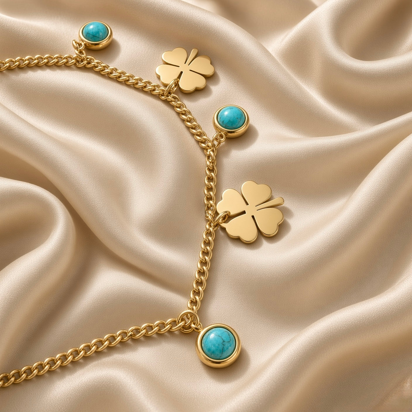 Gold Clover and Turquoise Charm Bracelet Curb Chain - macro detail on cream satin: bold gold curb chain showing flat mirror-polish gold four-leaf clover charm with four heart-shaped petals and engraved centre, round turquoise cabochon bezel charm with vivid sky blue-green stone and natural matrix markings in gold bezel