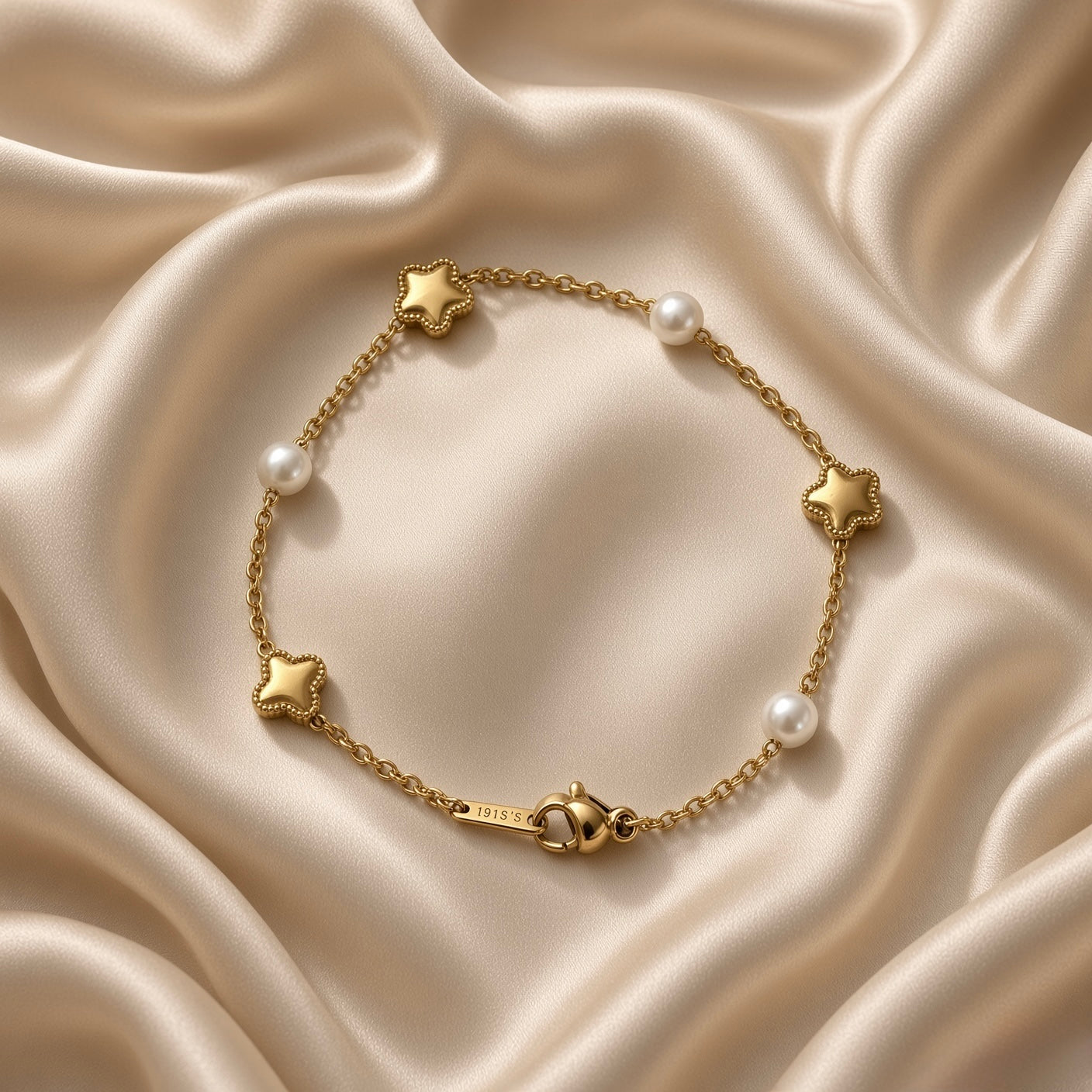 Gold Star and Pearl Station Bracelet Milgrain - circular flat lay on cream satin alternate angle: six-station bracelet in loop showing three puffy gold milgrain star charms and three round white pearl inline stations on fine gold cable chain, lobster clasp with engraved gold bar tag at bottom centre