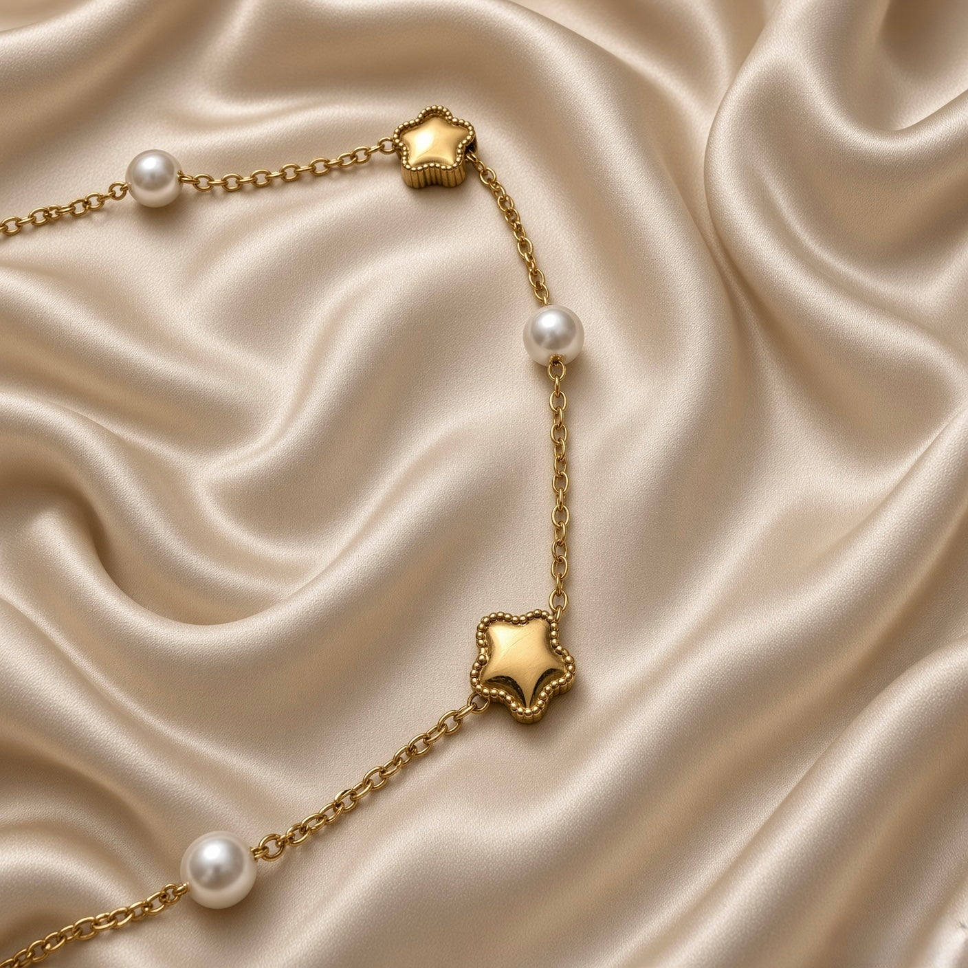 Gold Star and Pearl Station Bracelet Milgrain - vertical full-length flat lay on cream satin: complete bracelet laid straight showing all six stations, plain gold rectangular connector tab at top, three puffy milgrain gold star charms and three round white freshwater pearl stations along chain, lobster clasp with engraved gold rectangular bar tag at base
