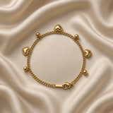 Gold Heart and Ball Charm Bracelet Milgrain Curb Chain - vertical full-length flat lay on cream satin: bold gold curb chain with six alternating dangle charms, three puffy milgrain-border gold heart charms and three smooth round gold ball charms, engraved gold tab at top, lobster clasp at base
